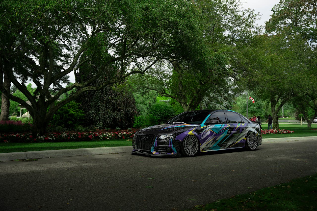 A custom sports car with unique graphics parked under lush greenery in a scenic urban park in Toronto.