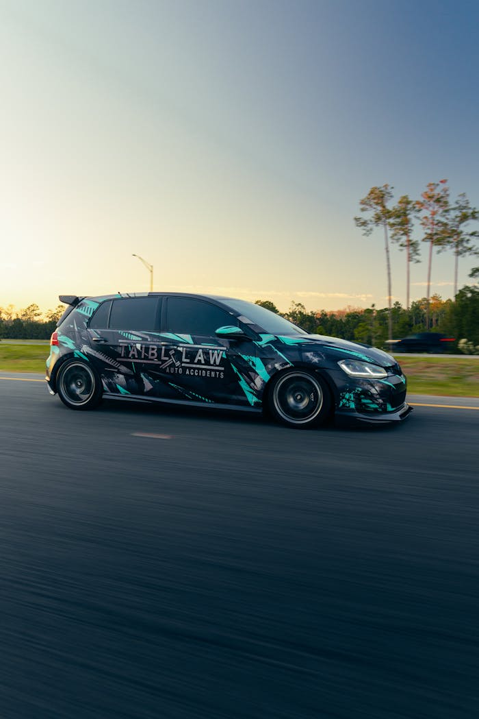 A sleek sports car with custom graphics speeds down a highway at sunset, showcasing its design.